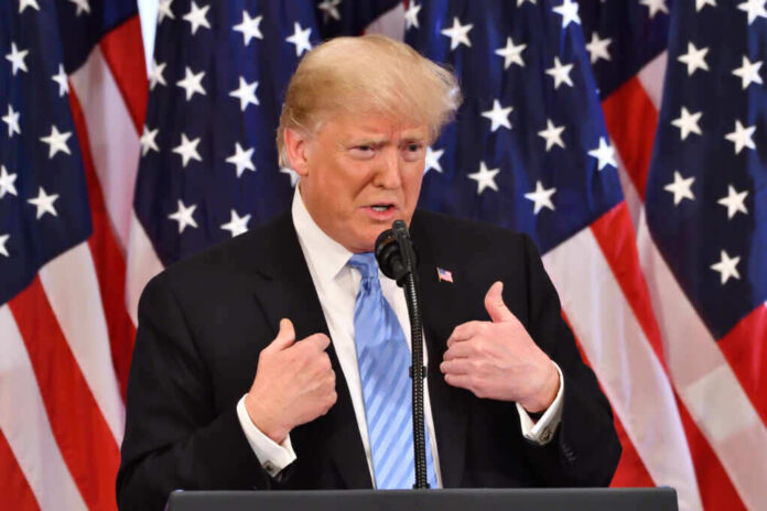 shutterstock_1200585187.jpg featured image Donald Trump speaking in front of multiple American flags.