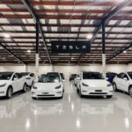 White Tesla cars displayed in showroom with Tesla sign.
