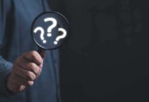 Hand holding magnifying glass with question marks inside.
