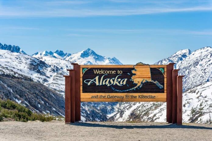 shutterstock_2164766705.jpg featured image Alaska welcome sign with snowy mountains in background