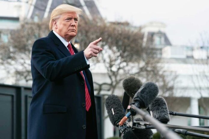 Man speaking to microphones, pointing outdoors.