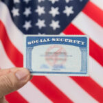 Hand holding social security card, American flag background.