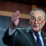 Chuck Schumer gesturing while speaking at a podium indoors.
