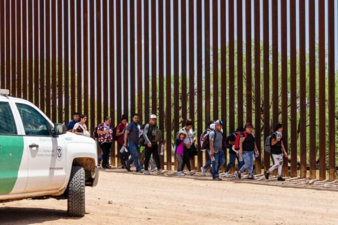 shutterstock_2333258557-1.jpg featured image Group of people walking by a border fence.