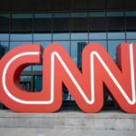 Red CNN logo in front of glass building.