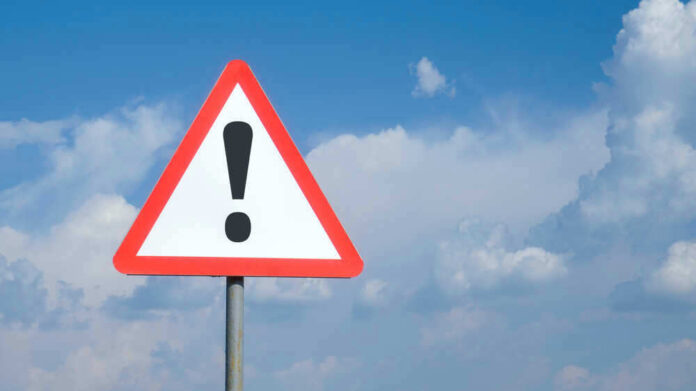 Triangle warning sign with exclamation mark against sky