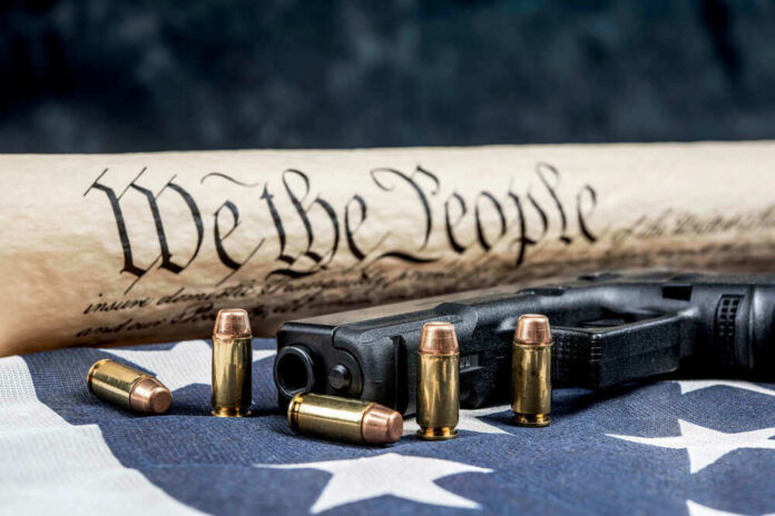 shutterstock_1864724608.jpg Gun and Constitution scroll on American flag
