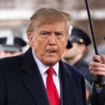 Donad Trump stands under an umbrella.