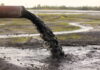 Pipe discharging black liquid onto muddy ground
