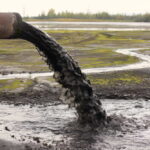 Pipe discharging black liquid onto muddy ground