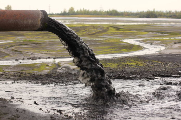 Pipe discharging black liquid onto muddy ground