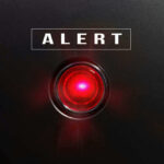 Red alert light against black background text ALERT