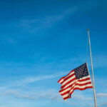 American flag at half-mast against a clear blue sky