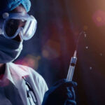 Person in PPE holding syringe with liquid droplets