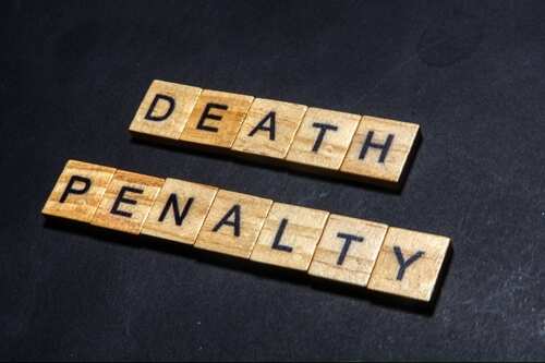 Wooden letter tiles spelling DEATH PENALTY on a dark background