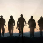 Five armed soldiers silhouetted against sunset background
