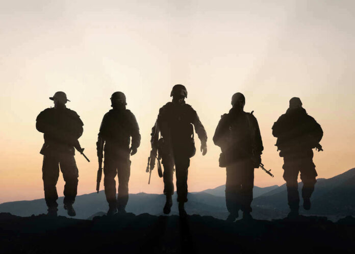 Five armed soldiers silhouetted against sunset background