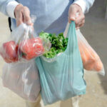 Person carrying grocery bags with vegetables and fruits