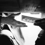 Hands passing money under a table, shrouded in mystery