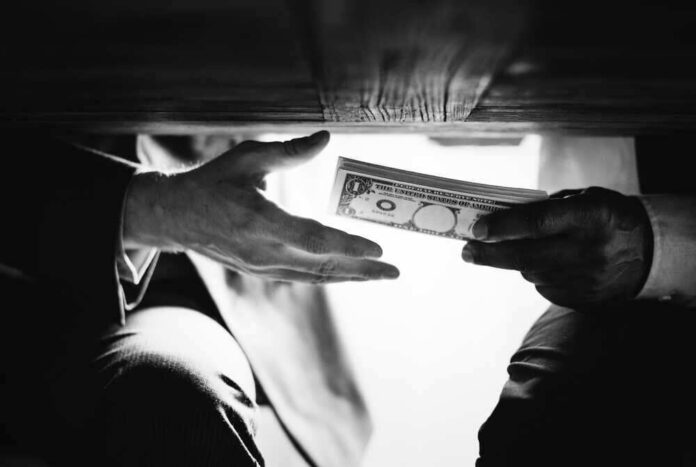 Hands passing money under a table, shrouded in mystery