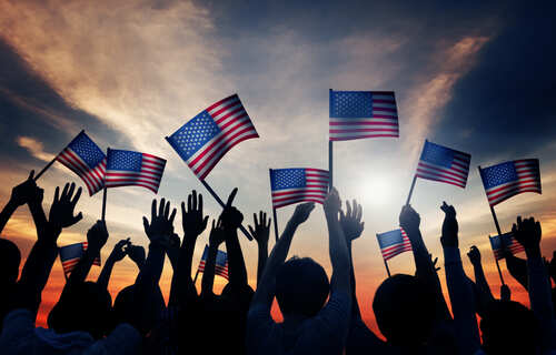 Silhouetted crowd holding American flags against a sunset