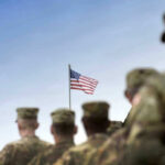 Soldiers in uniform facing American flag outdoors