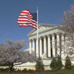 US Supreme Court building with an American flag and cherry blossom trees