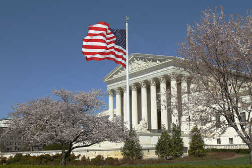 US Supreme Court building with an American flag and cherry blossom trees