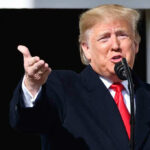 Person speaking into a microphone, gesturing with hand.