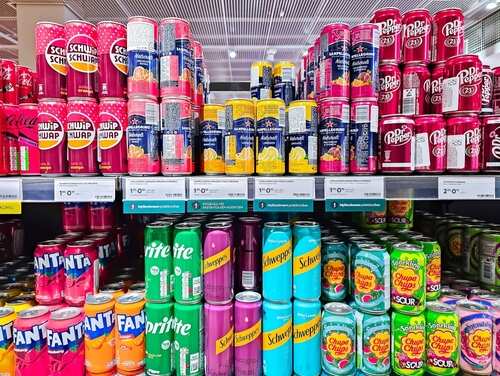 A variety of soda cans displayed on supermarket shelves