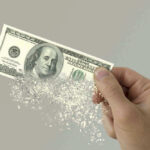 Hand holding a disintegrating hundred dollar bill.