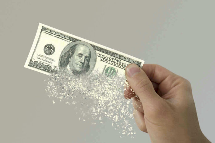 Hand holding a disintegrating hundred dollar bill.