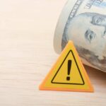 A roll of cash next to a warning sign on a wooden surface
