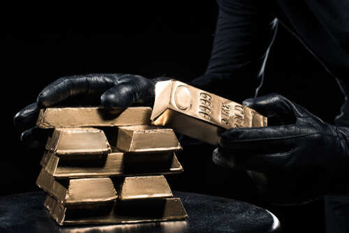 A person in black gloves handling gold bars against a dark background