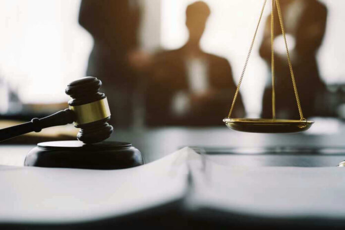 Gavel and scales in courtroom with blurred figures behind.