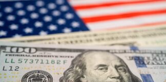 Close-up of a hundred dollar bill in front of an American flag