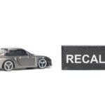 A miniature gray sports car next to a black sign that reads 'RECALL'