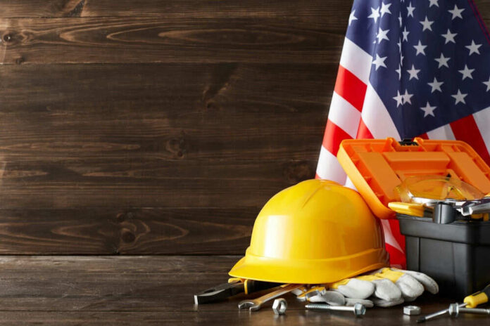 shutterstock_2347379367.jpg Yellow hard hat and tools with American flag.