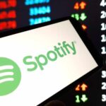 A smartphone displaying the Spotify logo in front of a stock market screen