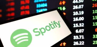 A smartphone displaying the Spotify logo in front of a stock market screen