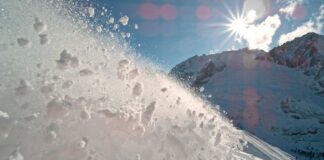 Snow spraying from a slope under a bright sun