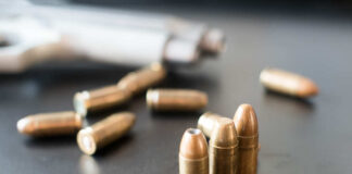 Close-up of bullets on a dark surface with a handgun in the background