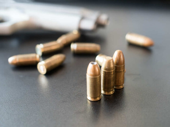 Close-up of bullets on a dark surface with a handgun in the background