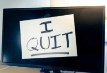 A computer monitor displaying a handwritten note that says 'I QUIT'