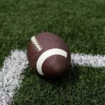 Former NFL Star Charged in Gruesome Murder A brown football resting on green artificial turf near a white line