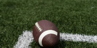 A brown football resting on green artificial turf near a white line