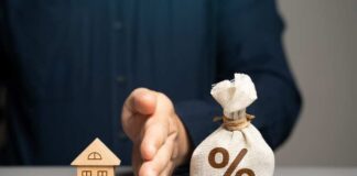 A wooden house model next to a money bag with a percentage symbol