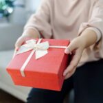 Person handing over a red gift box with a ribbon