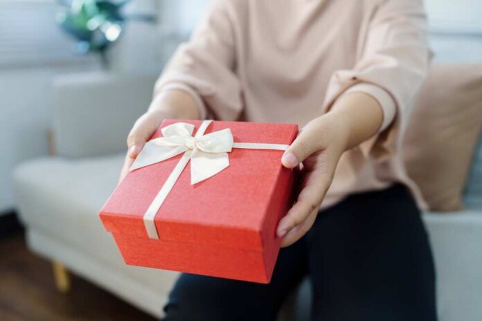 Person handing over a red gift box with a ribbon