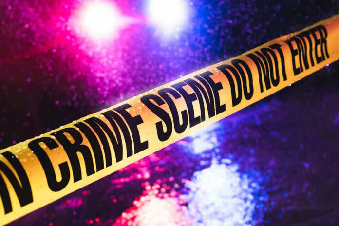 Crime scene tape with flashing lights in background.